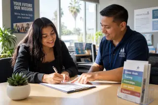 Young woman and adviser collaborating at a desk in a welcoming, sunlit office, both engaged and smiling.