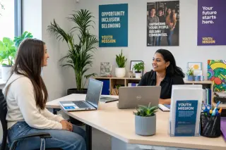 Young woman and counselor discussing opportunities at a bright, welcoming mission locale office with laptops and supportive décor.