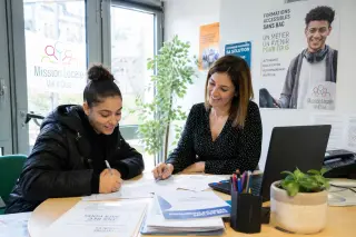 Young woman and counselor collaborating at a desk in a bright, welcoming Mission Locale office, discussing training opportunities in a positive and supportive atmosphere.